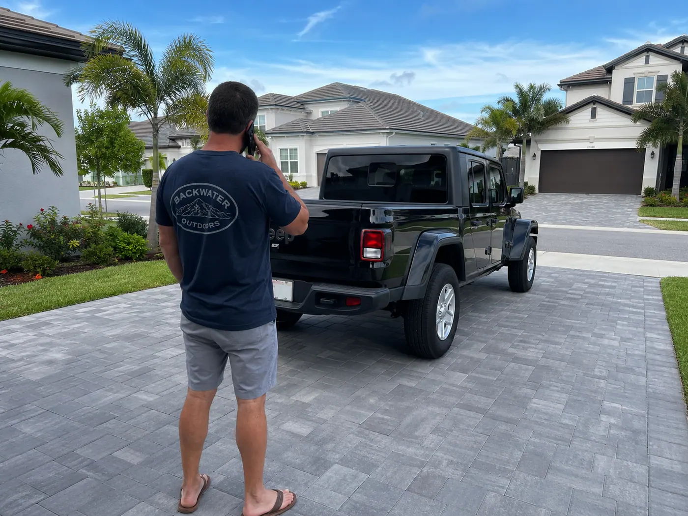 SunCoast team member in Backwater Outdoors shirt on the phone next to a black Jeep Gladiator in a Florida driveway