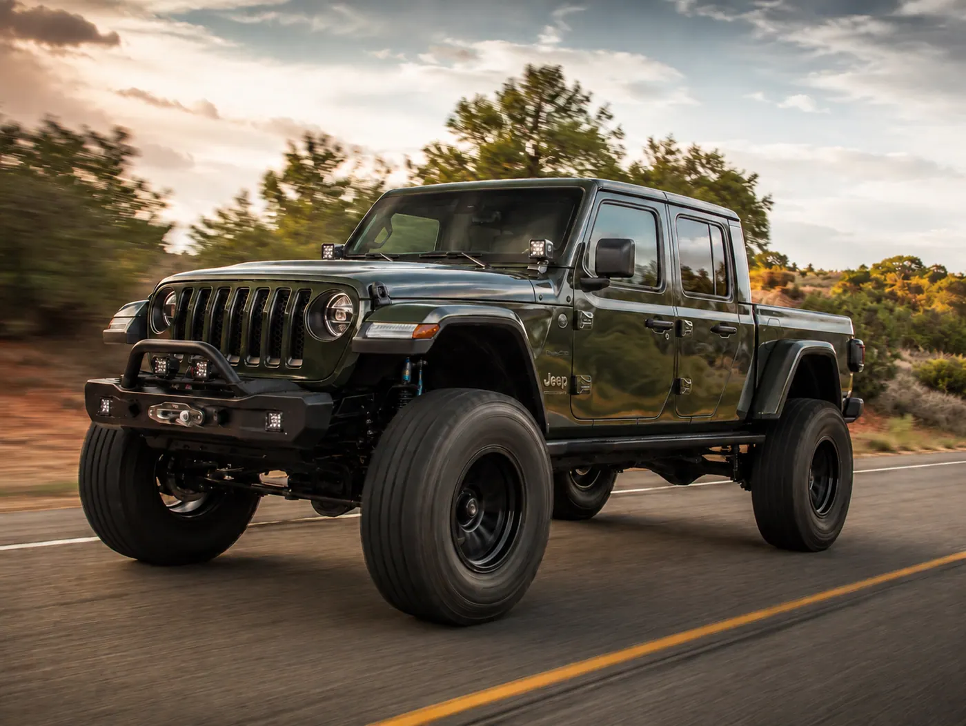 Lifted green Jeep Gladiator driving down a desert highway at sunset